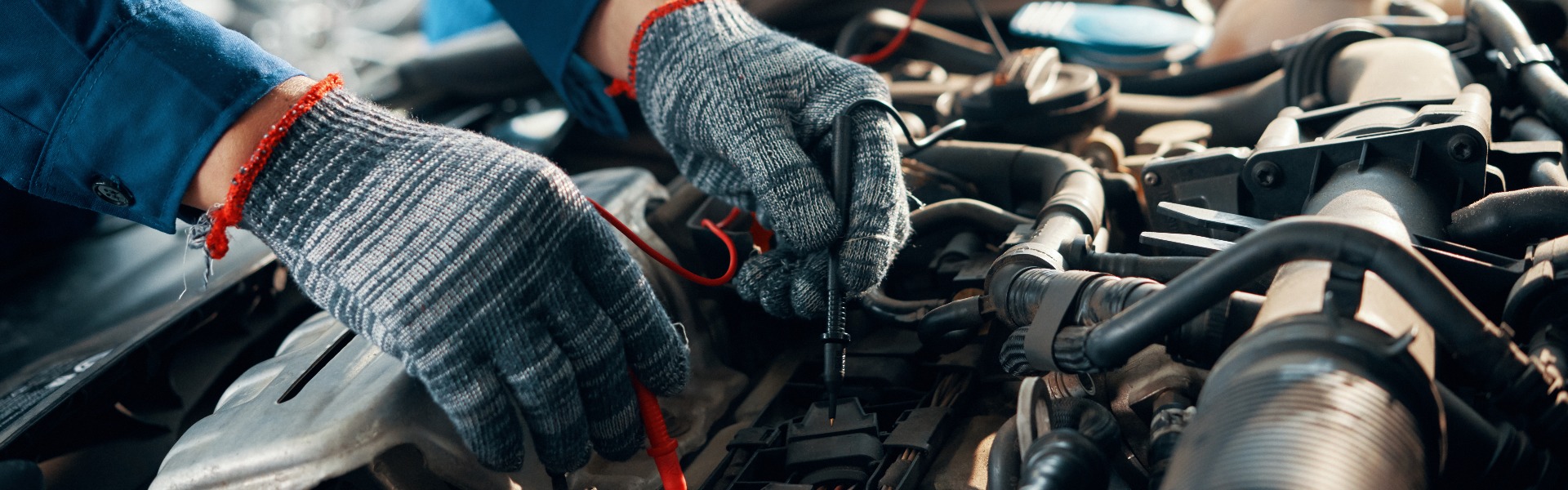 Close-up image of mechanic wearing protective gloves when using multimeter for testing automobile battery