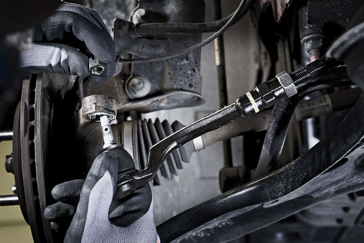 Eine Person mit grauen Handschuhen arbeitet konzentriert an einem schwarzen Autoteil