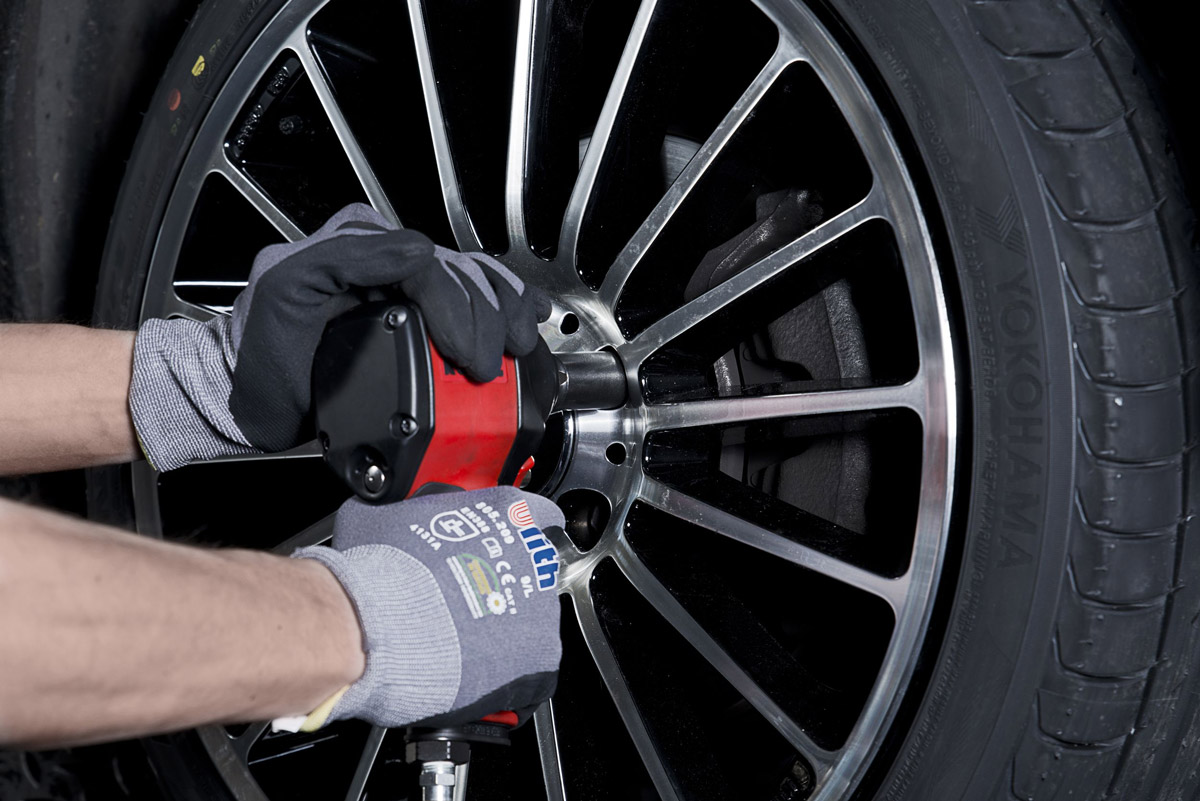 Eine Person mit Handschuhen montiert konzentriert ein silbernes Rad an einem Auto