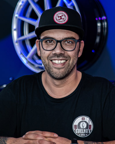 Ein Mann mit schwarzem Shirt und Mütze sitzt vor einem großen silbernen Rad