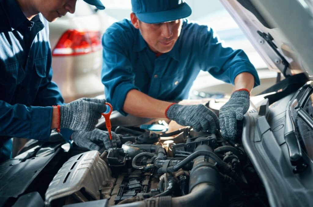 Mechanic measuring level of motor oil when his coworker checking pipes