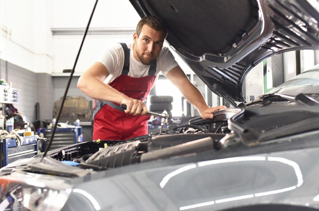 Portrait KFZ-Mechaniker repariert Auto in einer Werkstatt // Car mechanic repairs car in a workshop