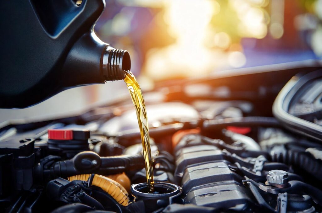 Pouring oil motor car lubricant from black bottle on engine background , service oil change auto repair shop; concept of petrochemical cleaning technology